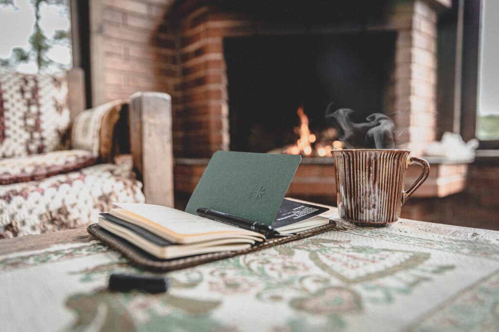 Notebook on a wooden table with a log burning fire in the background to help you stay warm without electricity
