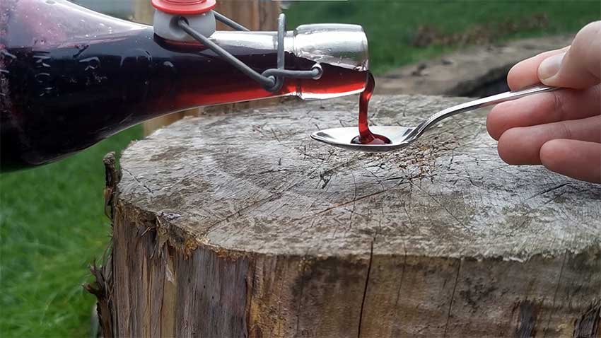 Elderberry syrup being poured onto spoon over a wooden log: how to make elderberry cough syrup